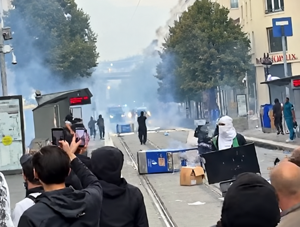 Manifestants et casseurs au milieu des fumigènes sur une voie de tramway, mobilier urbain renversé, lors des violences du 17 octobre
