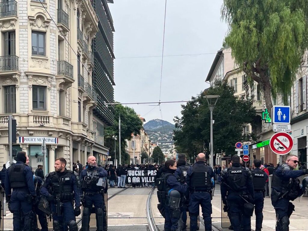 Cordon de policiers face à un cortège de manifestants avec une banderole, sur les voies du tramway dans le centre de Nice