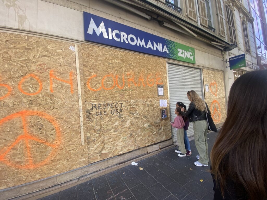 Messages de soutien écrits sur les panneaux de bois devant le magasin Micromania, avenue Jean-Médecin à Nice, avec deux passantes qui les lisent