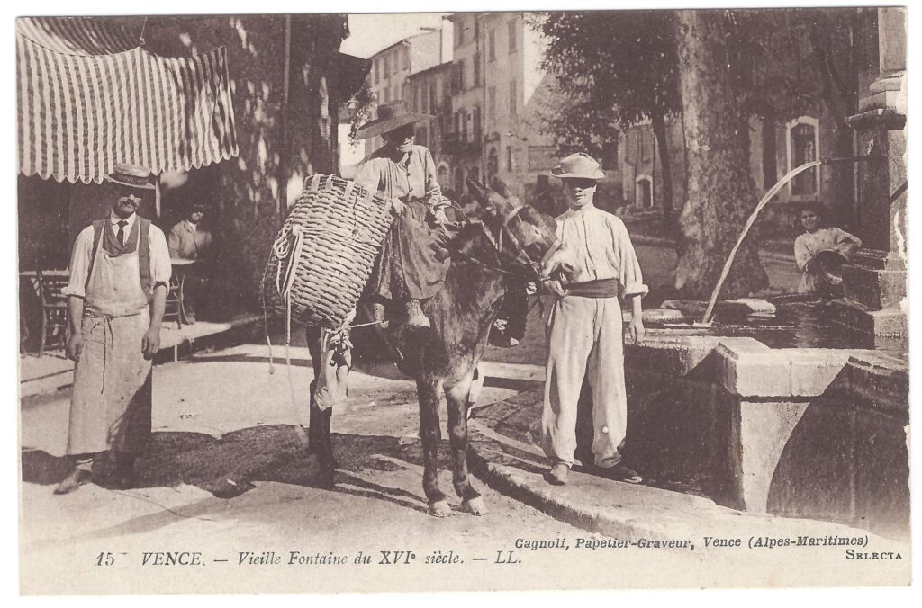 Carte postale ancienne de la vieille fontaine du XVIe siècle à Vence : un âne chargé d'un grand panier d'osier, entouré de deux hommes